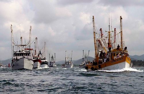 Barcos pesqueros en un mar agitado bajo un cielo nublado, con un gran arrastrero naranja en primer plano.