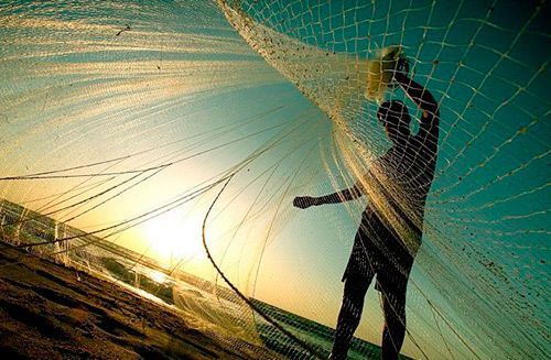 Silueta de una persona sosteniendo una red de pesca al atardecer en una playa