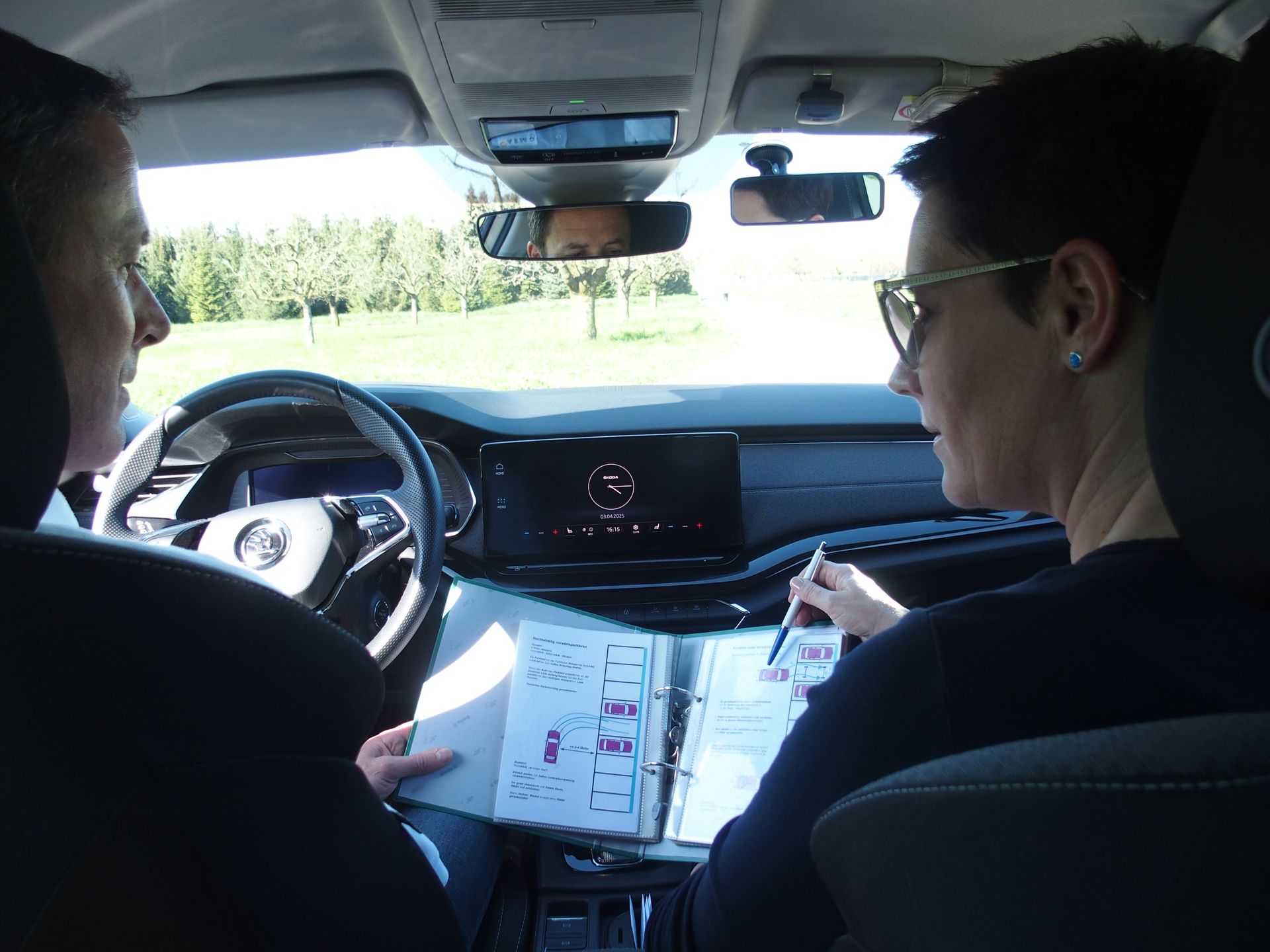 Eine Frau macht in einem Auto ihre Fahrprüfung, während ein Mann auf einem Klemmbrett schreibt.