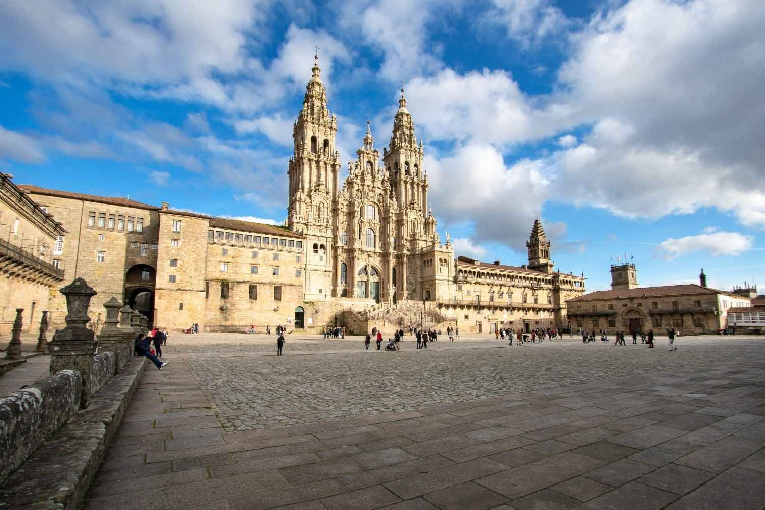 La ornamentada fachada de piedra y las dos torres de la catedral de Santiago de Compostela dan a una soleada plaza empedrada.