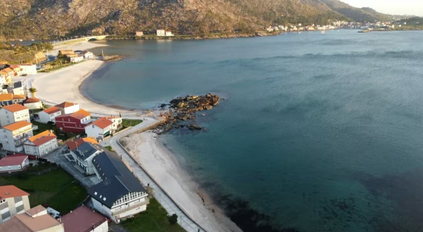 Vista aérea de una playa de arena que serpentea a lo largo de un pueblo costero con casas.
