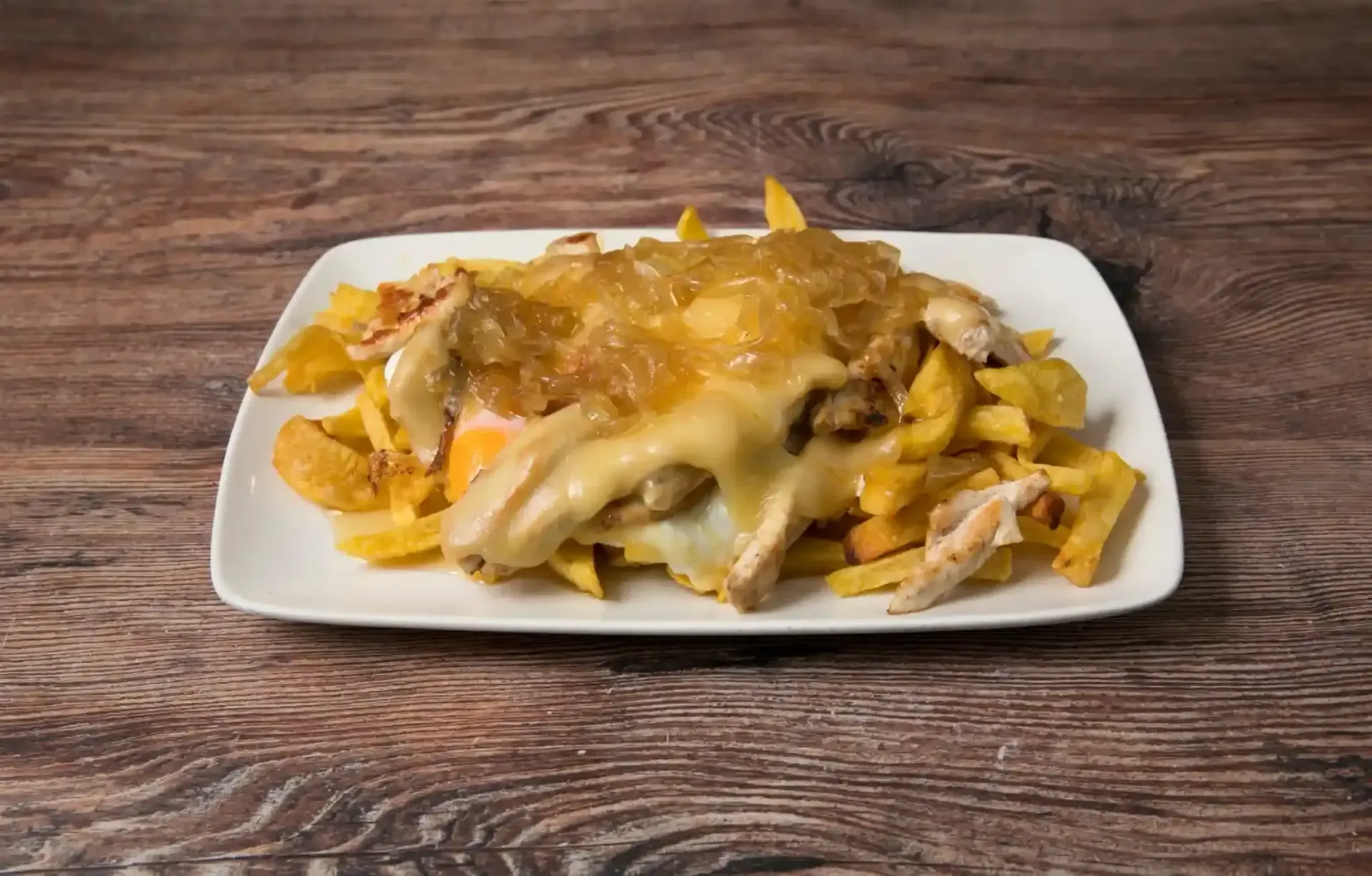 Pollo asado y patatas fritas en un plato blanco, colocado sobre una mesa de madera.