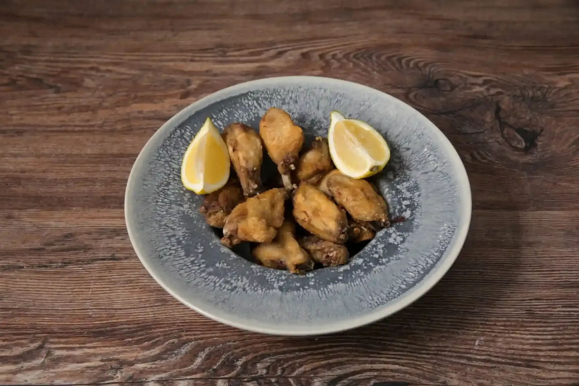 Alitas de pollo en un plato gris con gajos de limón, colocado sobre una mesa de madera.