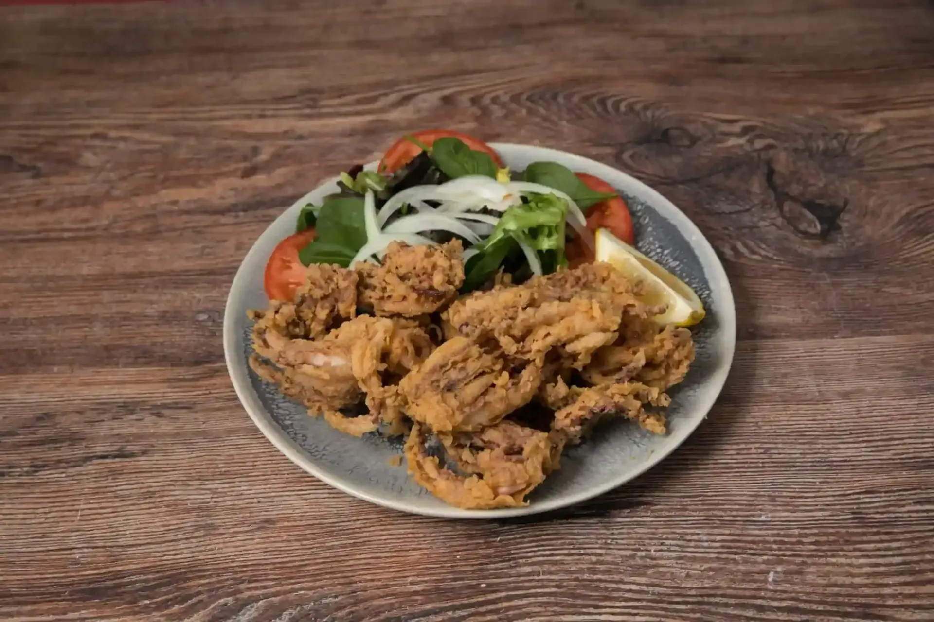Calamares fritos con ensalada y rodaja de limón en un plato, colocado sobre una mesa de madera.