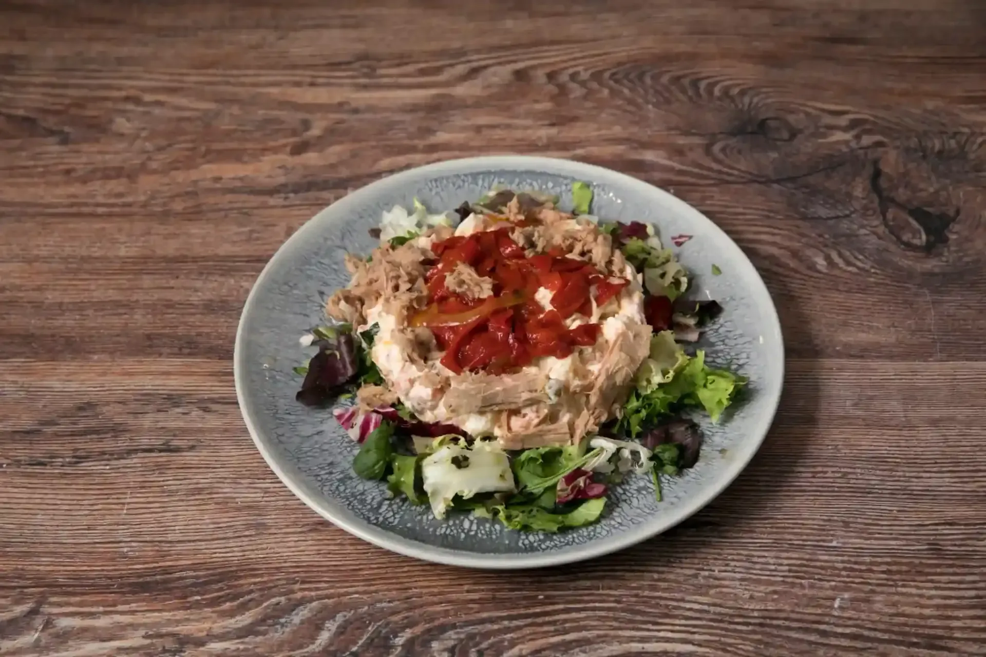 Ensalada de verduras mixtas, cubierta con una sustancia cremosa blanca y salsa roja, servida en un plato gris.