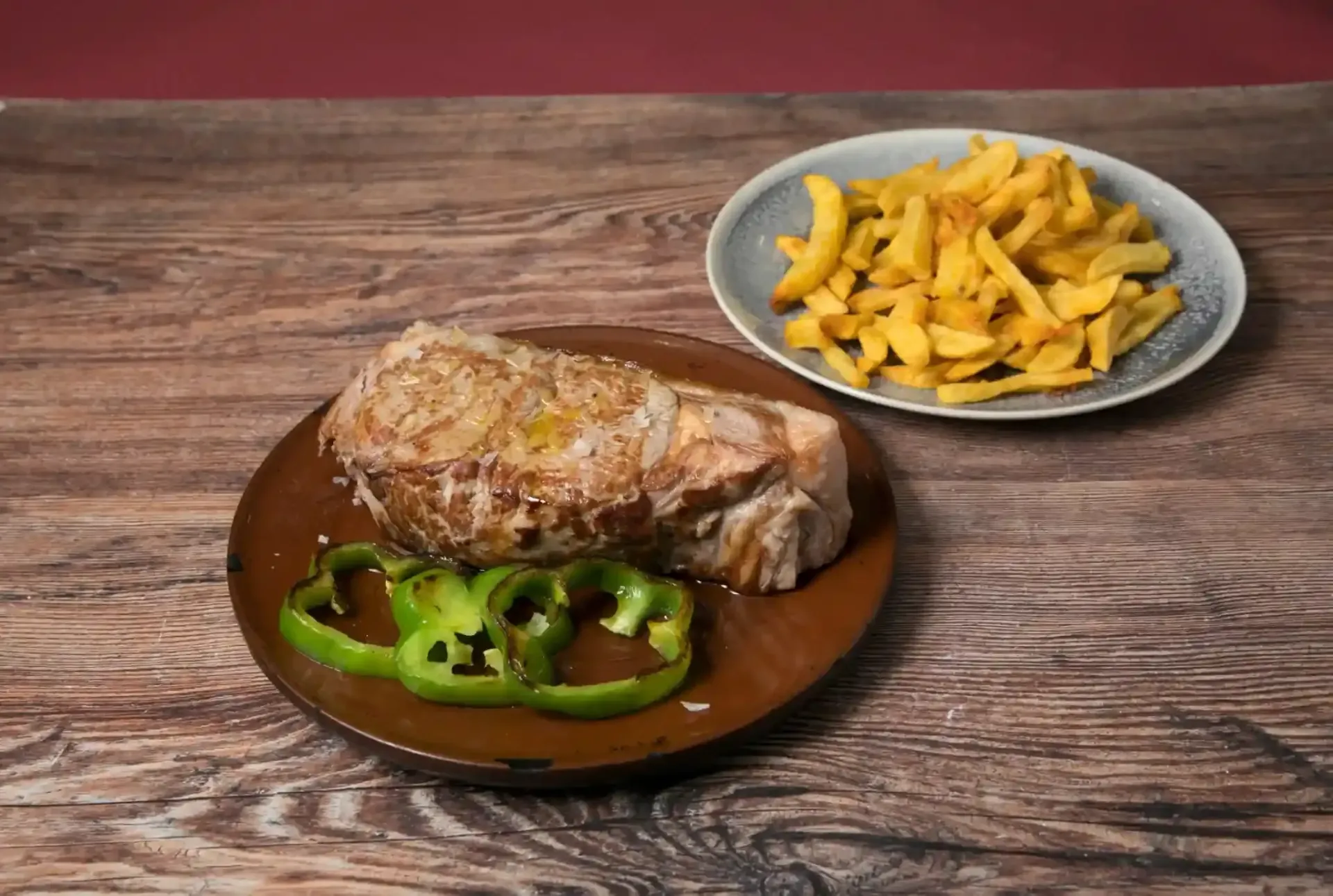 Menú de bistec y papas fritas: bistec en un plato con pimientos en rodajas y papas fritas como acompañamiento, todo sobre una mesa de madera.