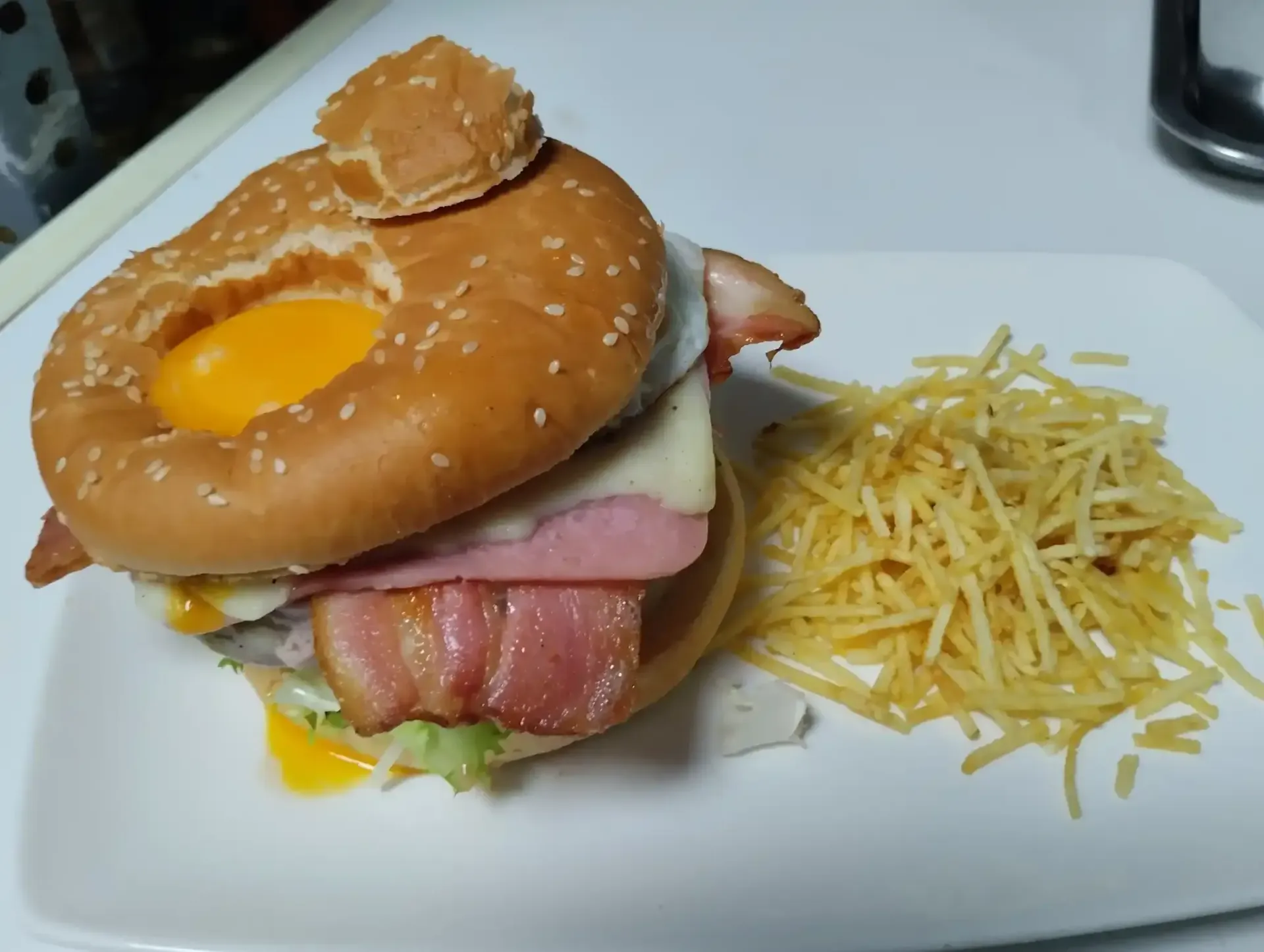 Hamburguesa con huevo, tocino y palitos de patata en un plato blanco.