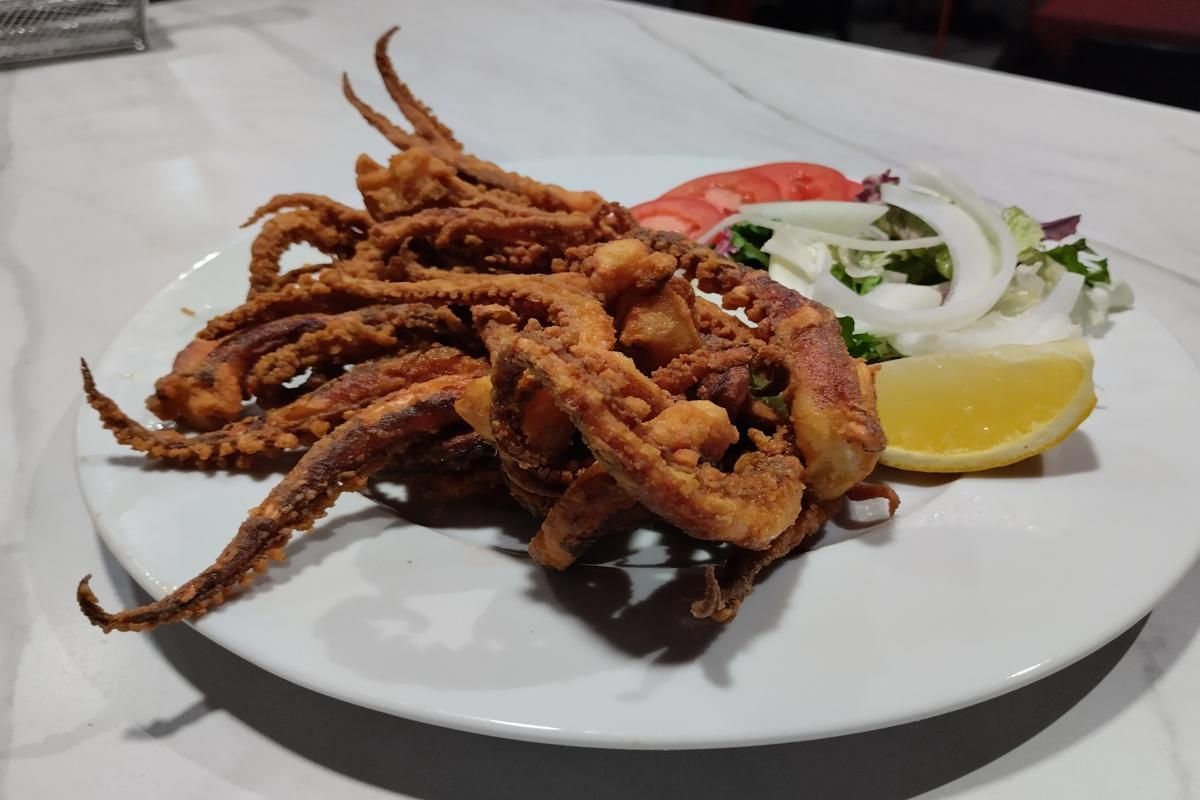Tentáculos de calamar fritos en un plato blanco con limón, tomate y cebolla.