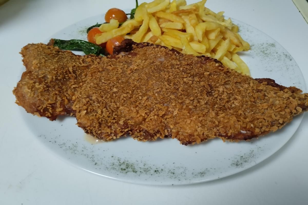 Chuleta rebozada con patatas fritas y tomates en un plato blanco.