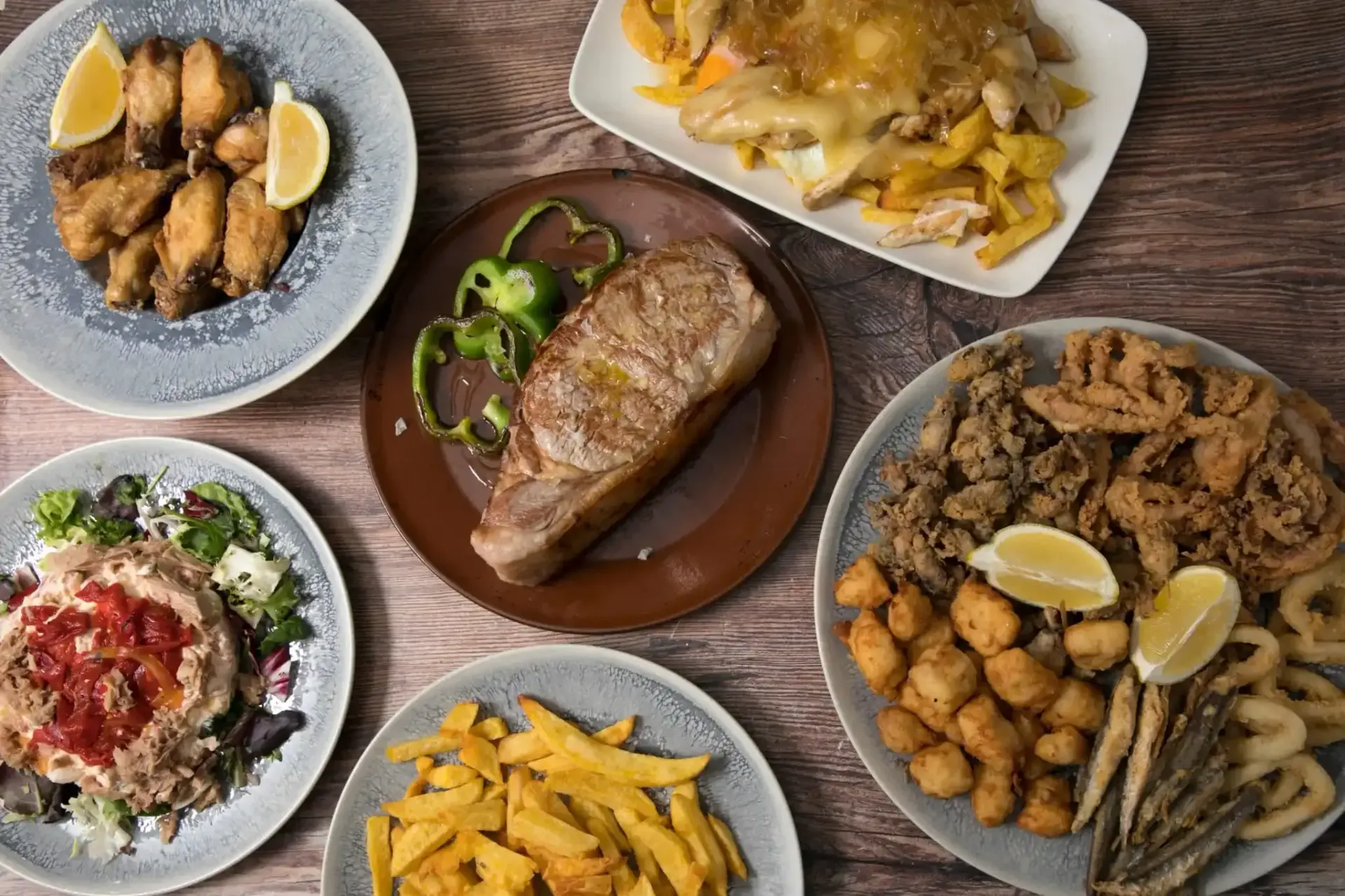 Vista aérea de varios platos de tapas españolas: alimentos fritos, filetes y verduras en platos.