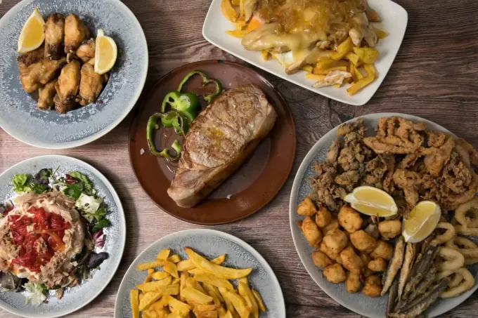 Vista aérea de varios platos de tapas españolas: alimentos fritos, filetes y verduras en platos.