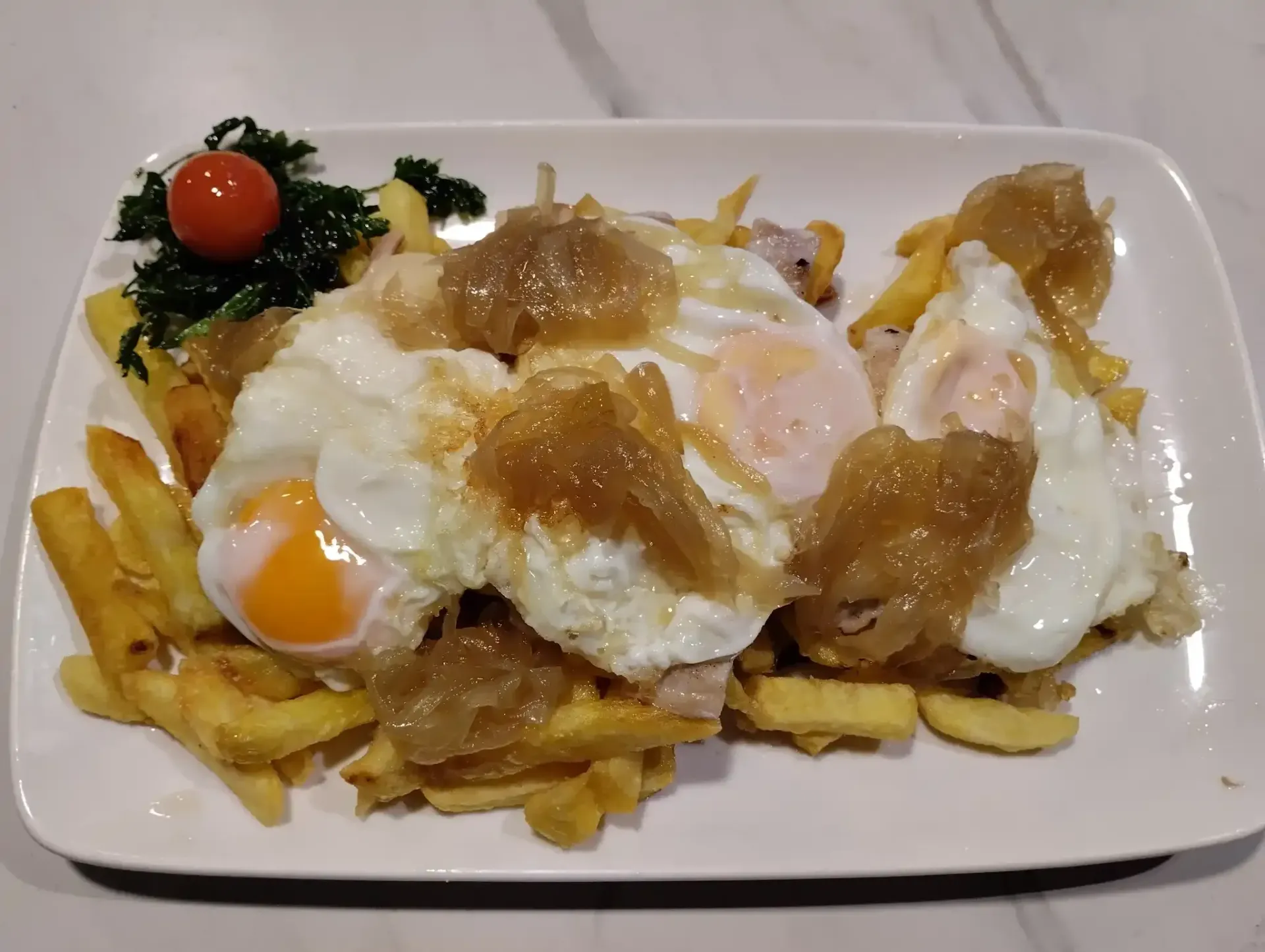 Plato de patatas fritas con huevos fritos y salsa, con guarnición.