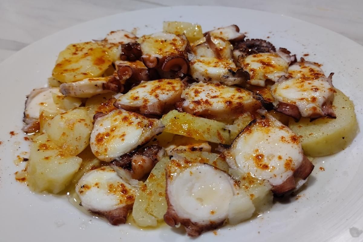 Pulpo y patatas con pimentón en plato blanco.