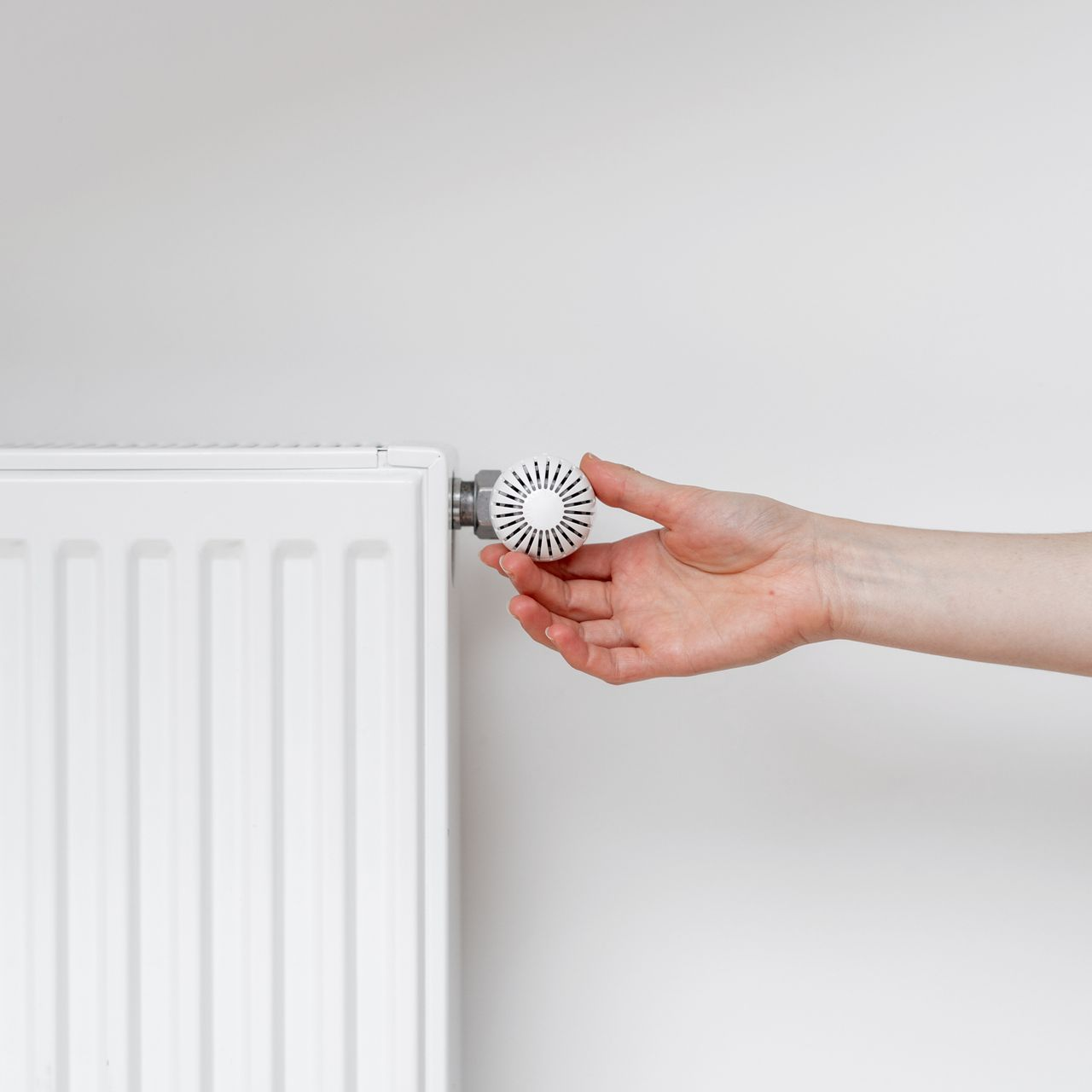 Une main ajuste le bouton d'un radiateur mural blanc, adossé à un mur blanc uni.