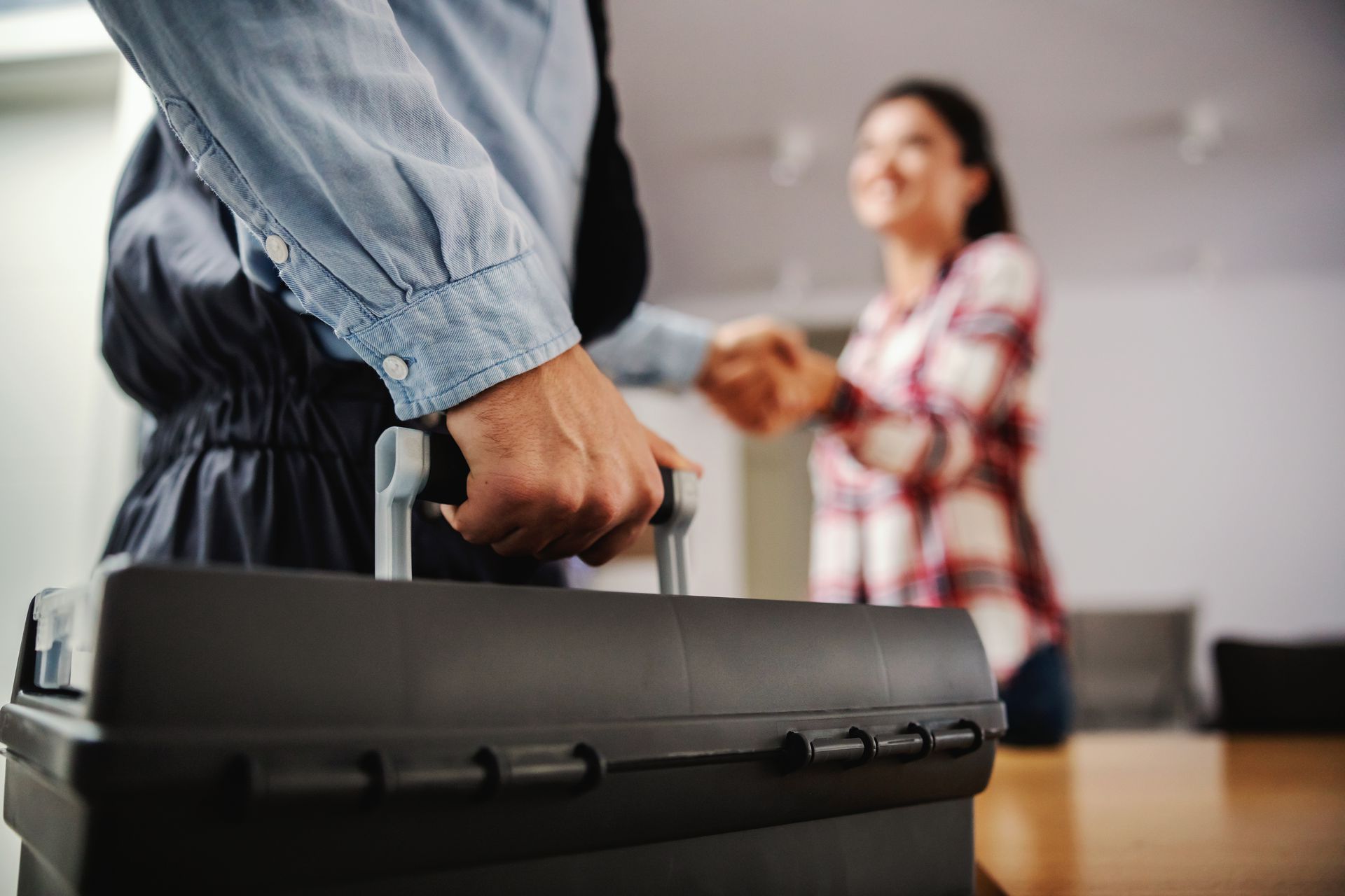 Handwerker trägt einen Werkzeugkoffer in der einen Hand und schüttelt mit der anderen die Hand der Kundin
