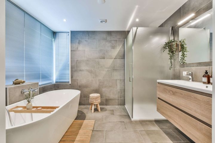Modernes helles Badezimmer mit ebenerdiger Dusche und Waschbecken auf der rechten Seite und einer Badewanne unterm Fenster auf der linken Seite