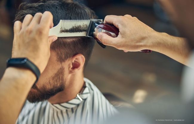 Ein Barbier schneidet einem Mann in einer Nahaufnahme im Salon die Haare mit Haarschneidemaschine und Kamm.