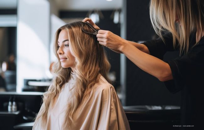Eine Frau lässt sich im Salon die Haare stylen, eine Stylistin kreiert sanfte Wellen.