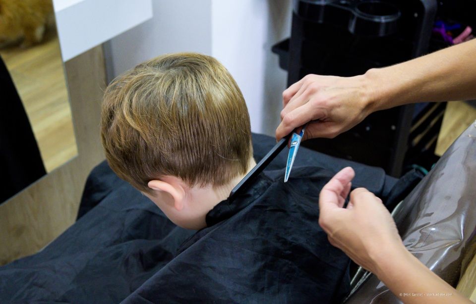 Eine Friseurin schneidet in einem Salon kurze blonde Haare mit einer Schere; die Kundin trägt einen schwarzen Umhang.