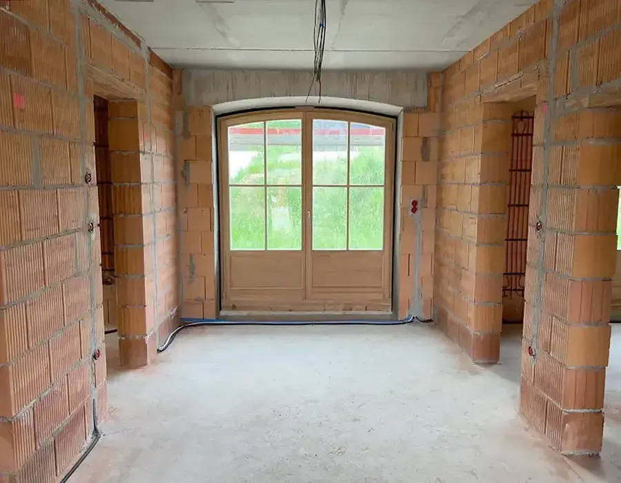 Eingangsbereich eines Neubaus im Rohbau mit eingebauter Haustür und unverputzten Ziegelwänden.