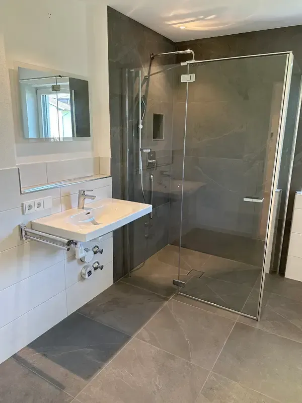 Modernes Badezimmer mit bodengleicher Glasdusche und großformatigen Wandfliesen.