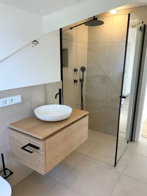Modernes Badezimmer im schlüsselfertigen Haus mit bodengleicher Dusche und Glasabtrennung.