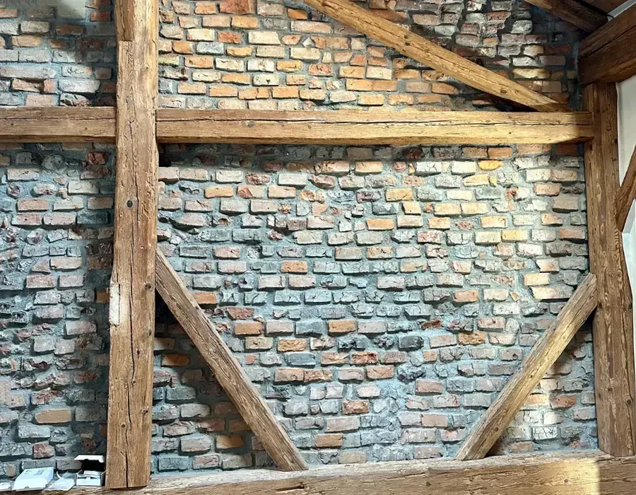Freigelegte historische Backsteinwand mit sichtbarer Holzbalkenkonstruktion im sanierten Bestandsgebäude.