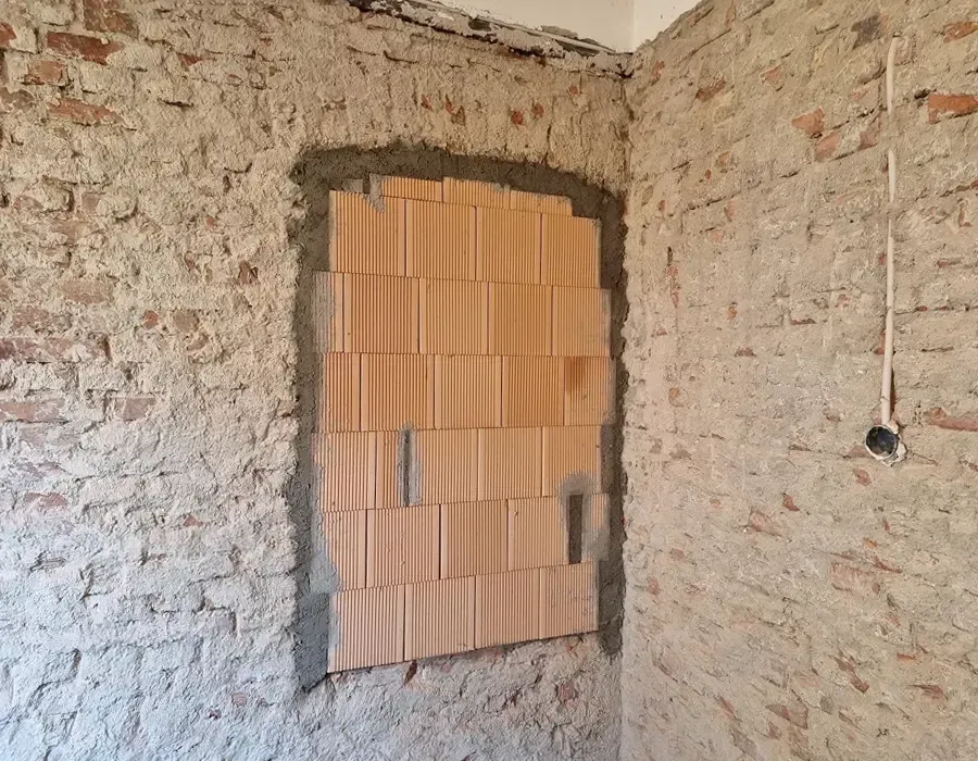 Teilweise verschlossene Wandöffnung in einer freigelegten historischen Mauer im Rohbauzustand.