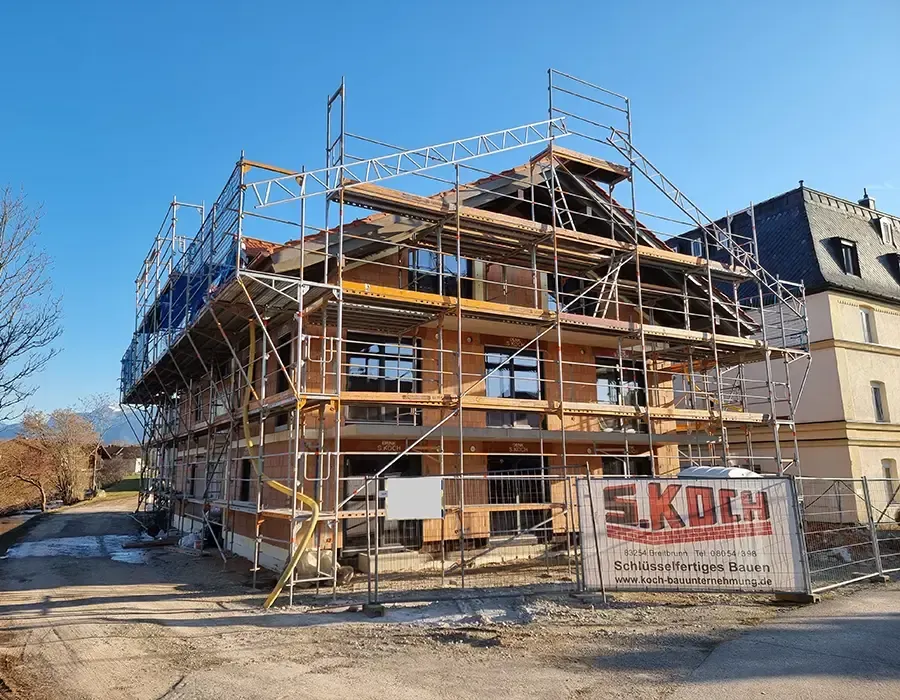 Wohnhaus-Neubau im Rohbau mit Gerüst und Dachkonstruktion unter blauem Himmel.