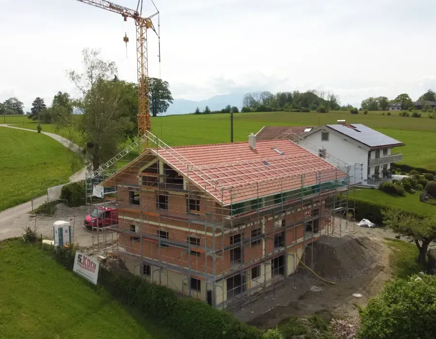 Luftaufnahme eines Wohnhaus-Neubaus mit fertig eingedecktem Dach im ländlichen Umfeld.