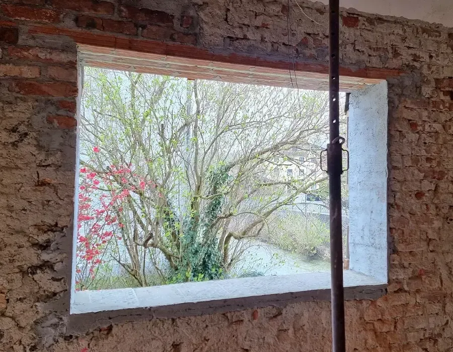Fensteröffnung in einer sanierten Backsteinwand mit Blick auf einen Baum im Garten.