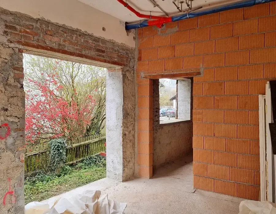 Neu geschaffene Wandöffnung und Ziegelmauerwerk im Umbau mit Blick nach draußen auf einen blühenden Baum.