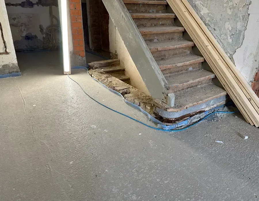 Rohbau-Treppenhaus mit Betontreppe, freiliegenden Leitungen und unfertigen Wandflächen.