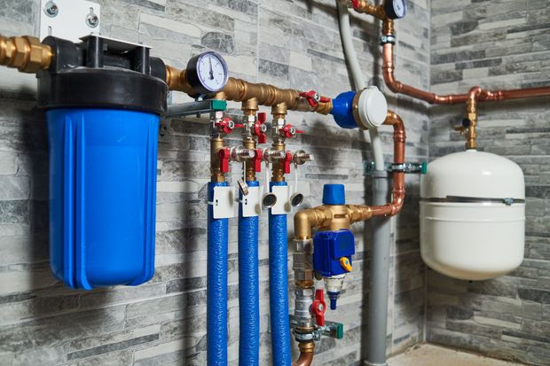 Hauswirtschaftsraum mit blauer Wasserfilteranlage, Manometern, Rohren und einem weissen Ausdehnungsgefäss an einer Betonwand