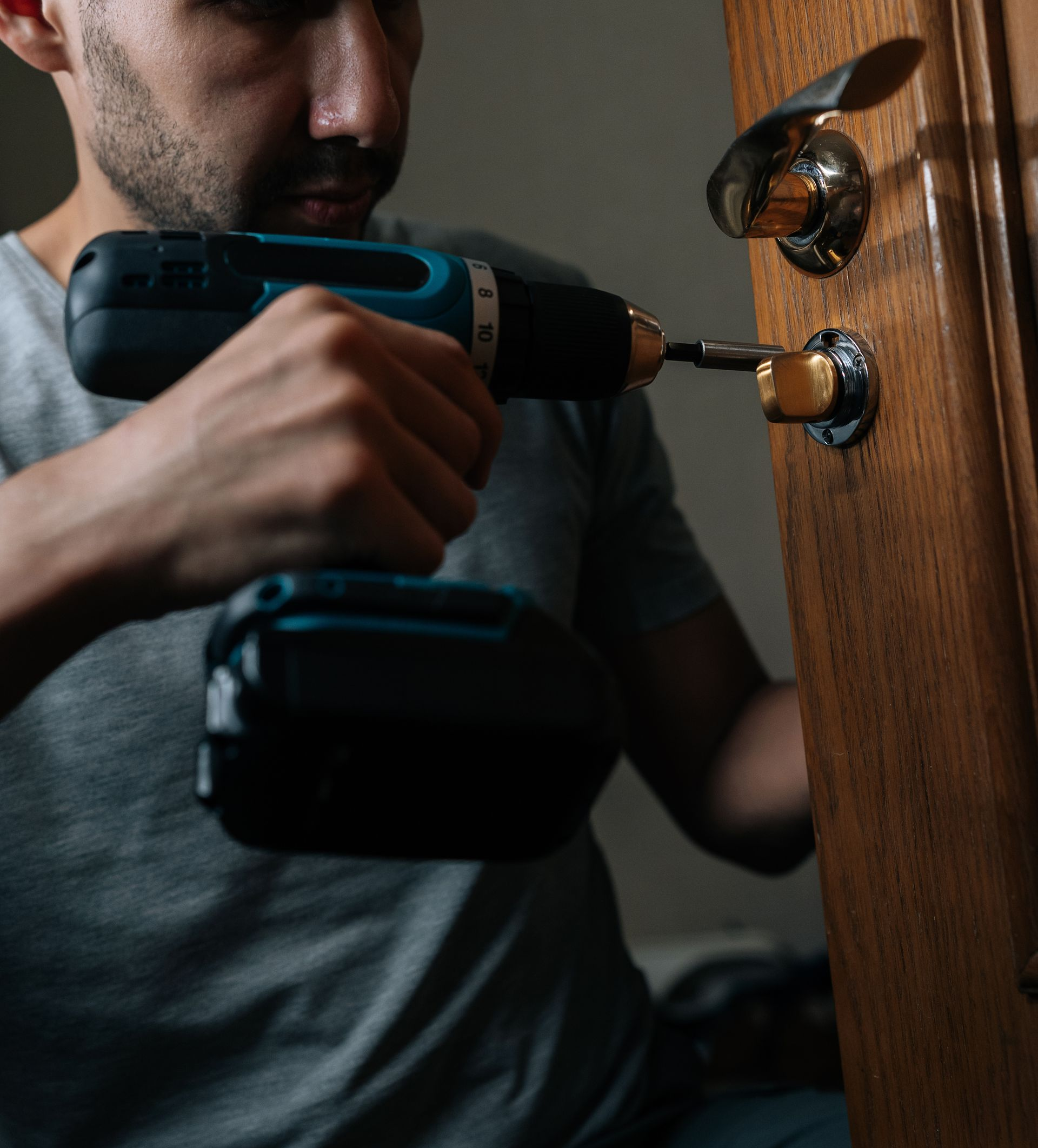 Une personne utilise une perceuse pour installer une serrure sur une porte en bois.