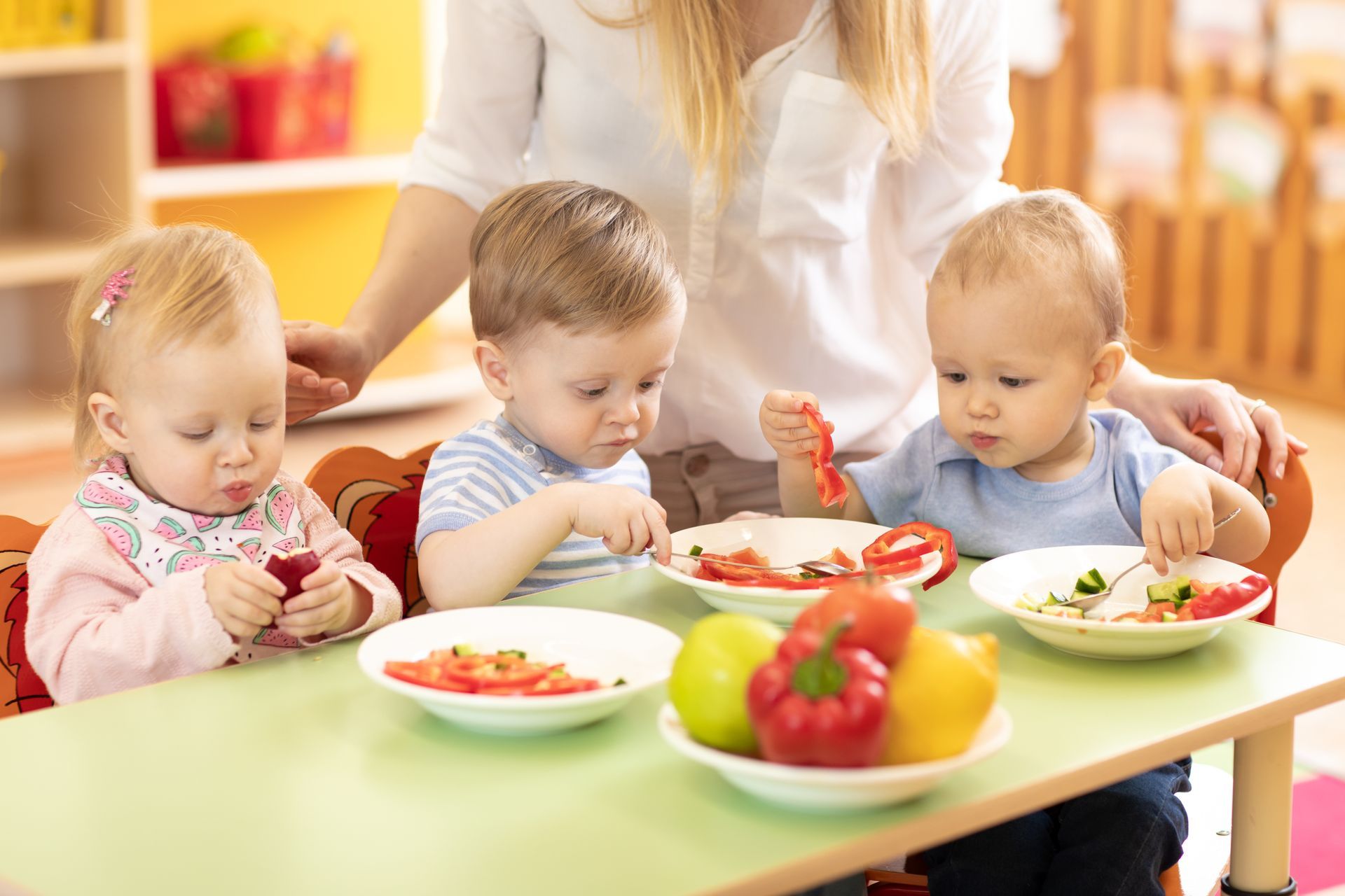 Un gruppo di bambini è seduto a un tavolo e mangia frutta e verdura.