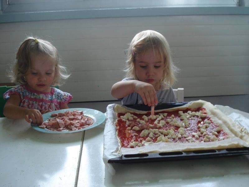 Due bambine stanno preparando una pizza con un piatto di pizza sullo sfondo