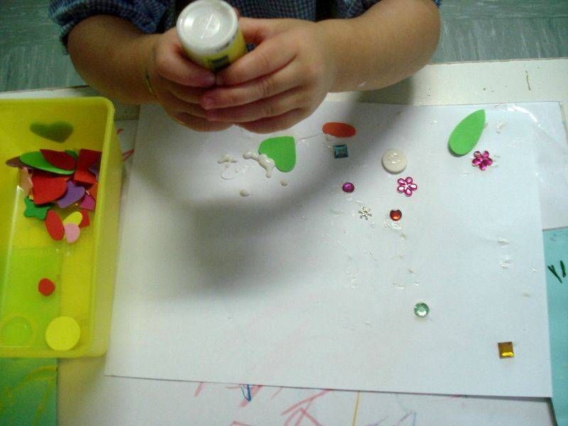 Un bambino tiene in mano una bottiglia di colla su un pezzo di carta