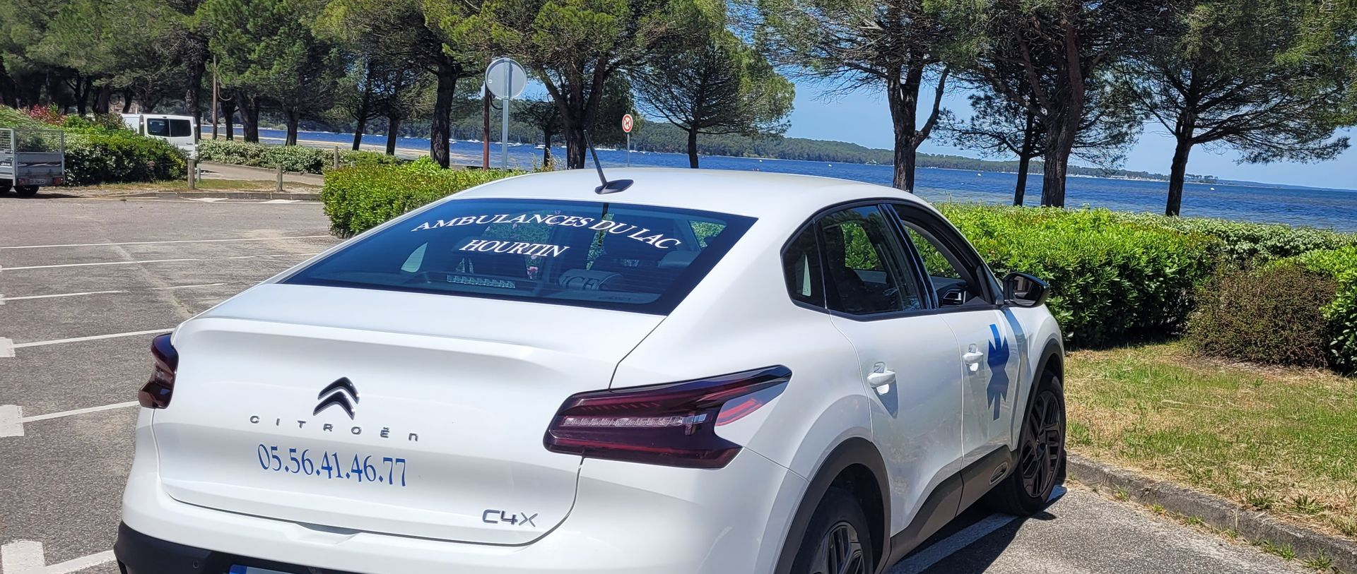 Une Citroën C4 à hayon garée sur un parking côtier, avec des arbres et de l'eau en arrière-plan.