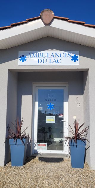 Entrée d'Ambulances du Lac avec une enseigne, des emblèmes de l'Étoile de Vie et des plantes en pot près de la porte.