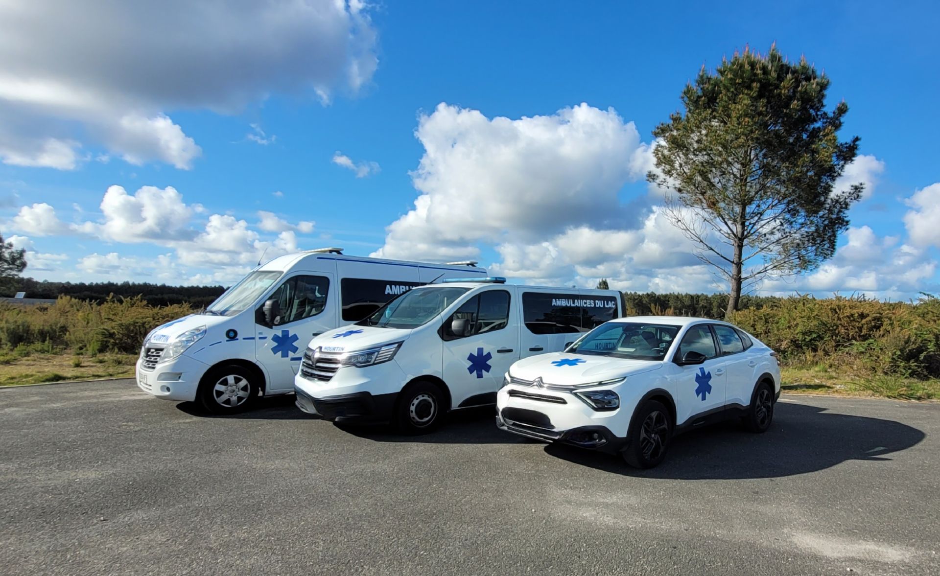 Trois véhicules de service médical étaient garés en rang sur un terrain de gravier.