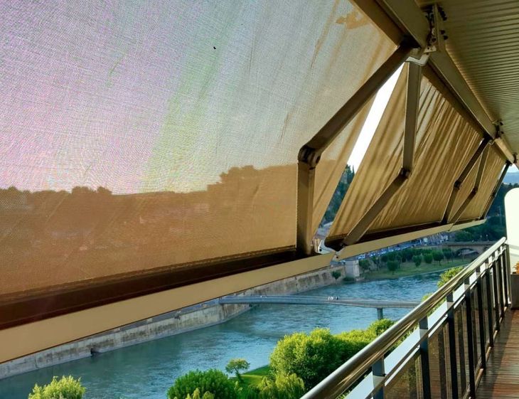Piscina al aire libre junto a una terraza sombreada, con velas de color beige y agua azul que refleja la luz del sol.