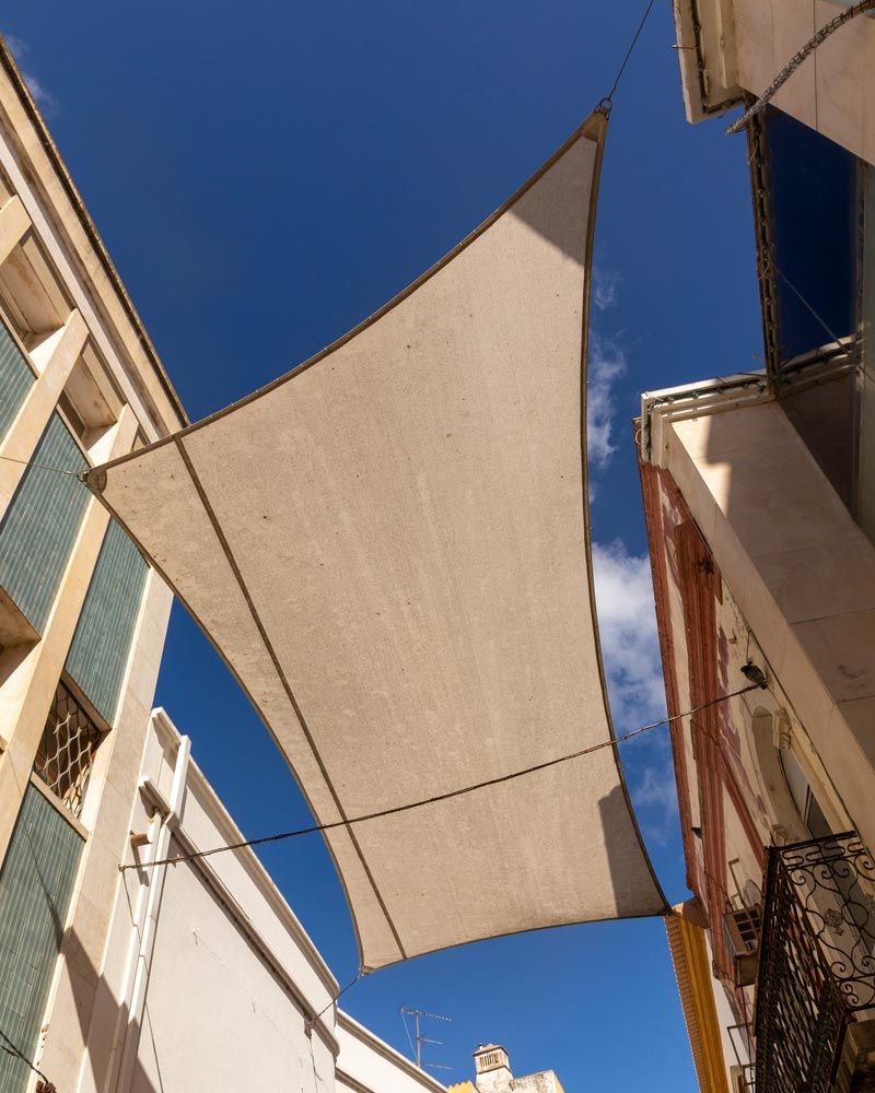 Toldos de sombra color beige se extendían entre los edificios sobre una calle estrecha contra un cielo azul.