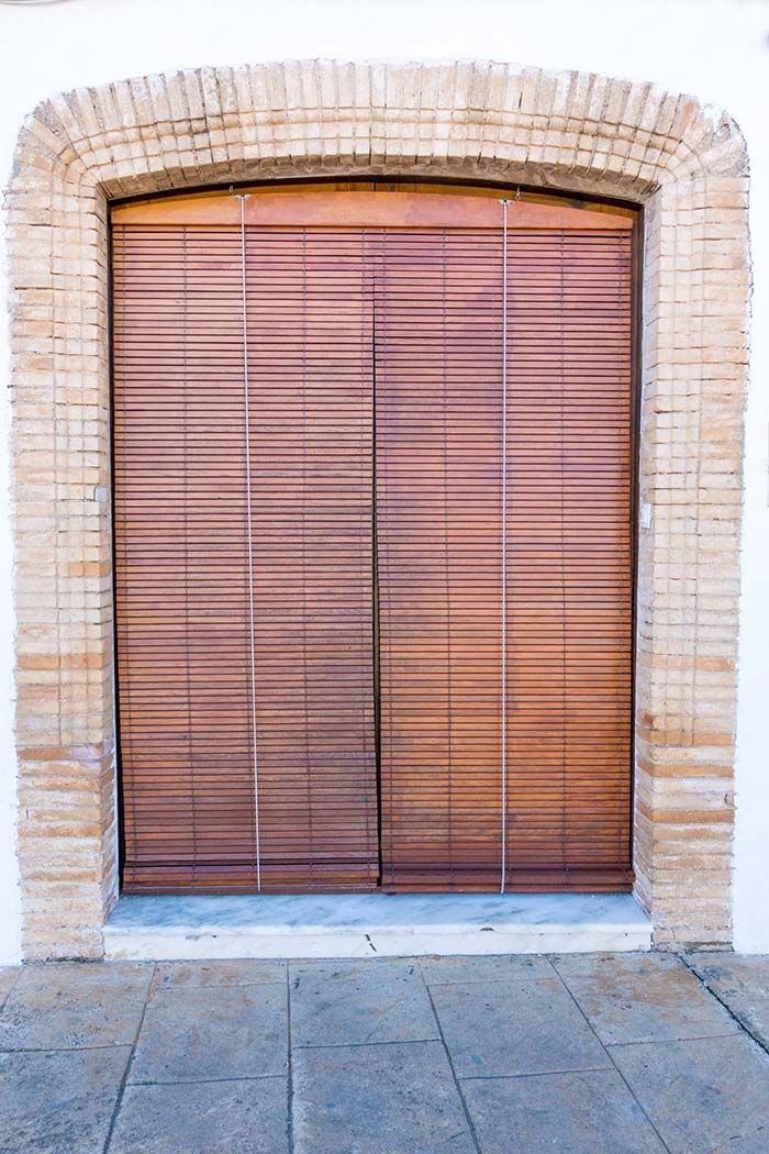 Puerta de madera cerrada de un local, con arco de ladrillo y un muro de piedra alrededor