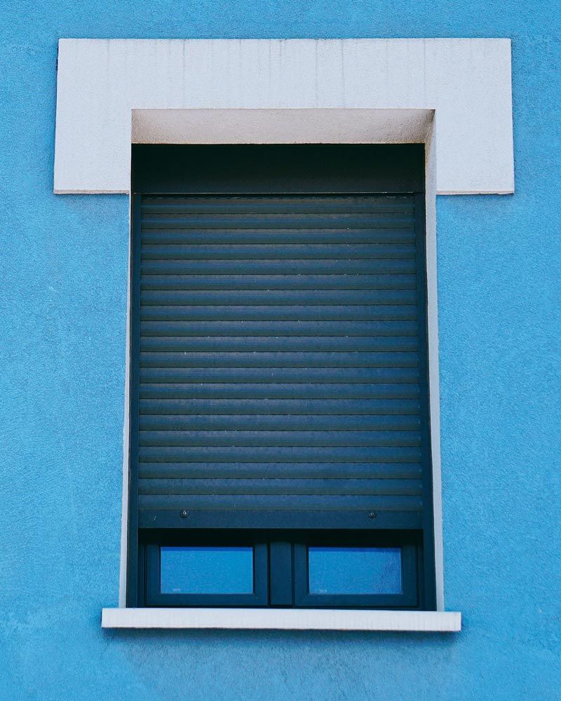 Pared azul con contraventana oscura cerrada y marco blanco.