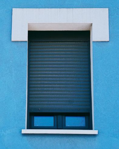 Pared azul con contraventana oscura cerrada y marco blanco.