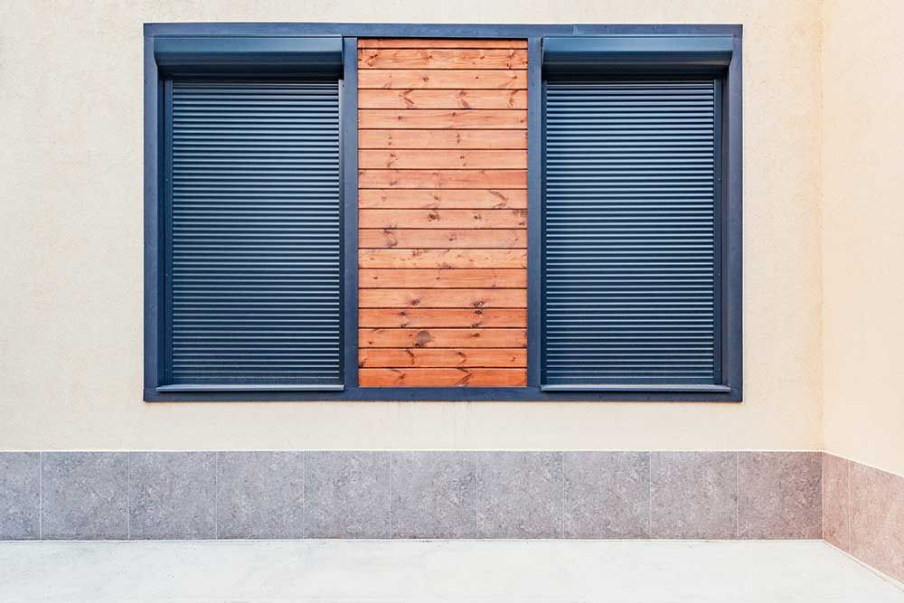 Ventana azul con postigos y un panel central de madera en una pared beige