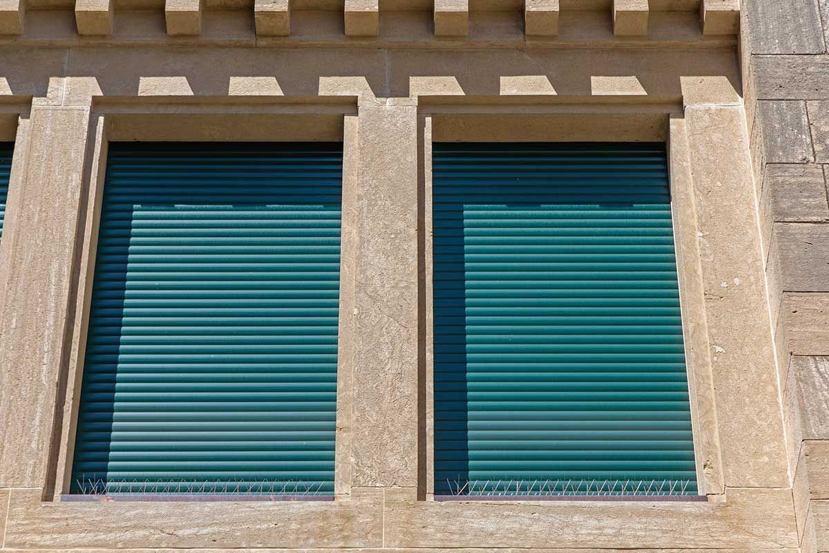 Dos contraventanas verde azulado en una fachada de piedra beige bajo una moldura decorativa