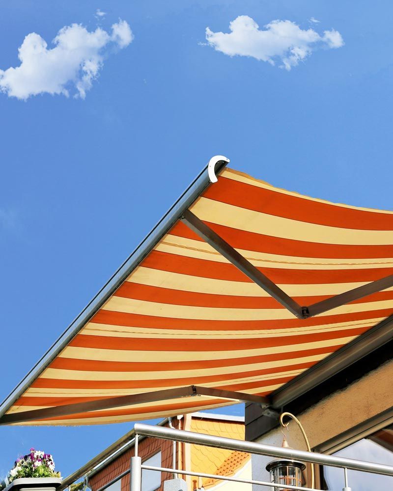 Toldo a rayas naranjas y crema contra un cielo azul con pequeñas nubes.
