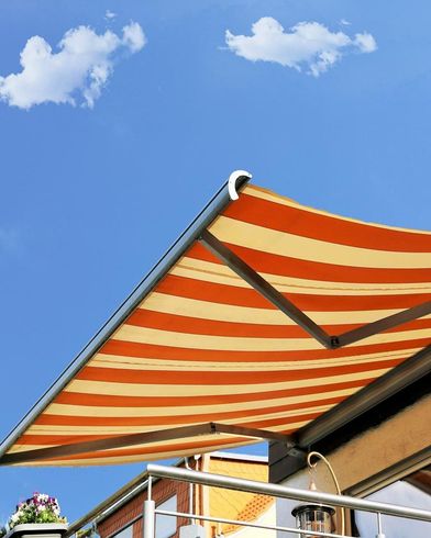 Toldo a rayas naranjas y crema contra un cielo azul con pequeñas nubes.